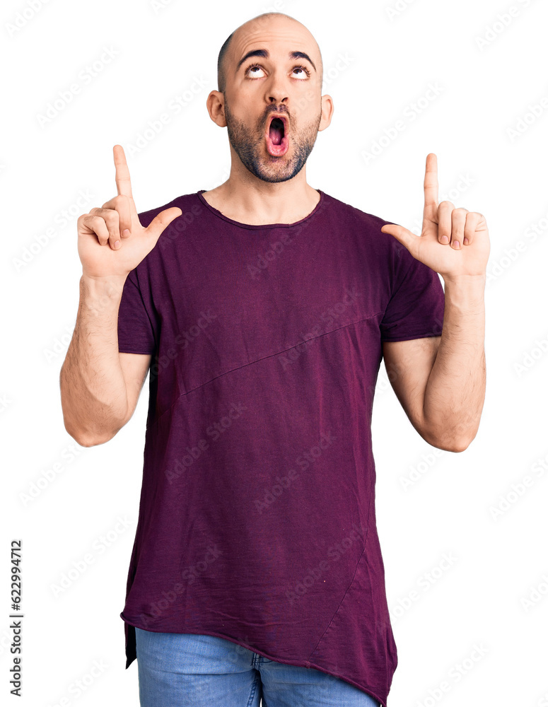 Canvas Prints Young handsome man wearing casual t shirt amazed and surprised looking up and pointing with fingers and raised arms.