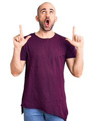 Young handsome man wearing casual t shirt amazed and surprised looking up and pointing with fingers and raised arms.