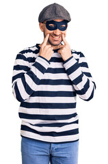 Young handsome man wearing burglar mask smiling with open mouth, fingers pointing and forcing cheerful smile