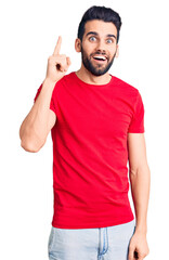 Young handsome man with beard wearing casual t-shirt pointing finger up with successful idea. exited and happy. number one.