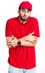 Young handsome man with beard wearing delivery uniform shaking and freezing for winter cold with sad and shock expression on face