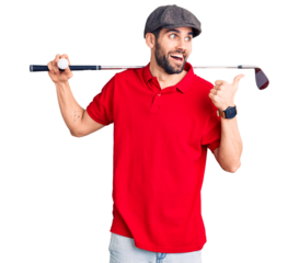 Young handsome man with beard playing golf holding club and ball pointing thumb up to the side smiling happy with open mouth