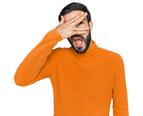 Young hispanic man wearing casual clothes peeking in shock covering face and eyes with hand, looking through fingers with embarrassed expression.