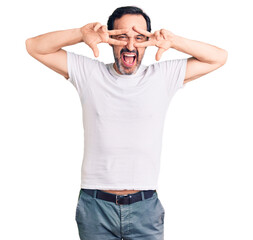 Fototapeta premium Middle age handsome man wearing casual t-shirt doing peace symbol with fingers over face, smiling cheerful showing victory