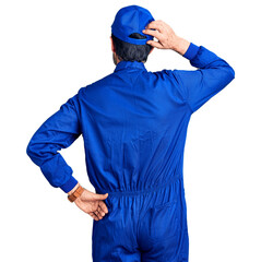 Middle age handsome man wearing mechanic uniform backwards thinking about doubt with hand on head