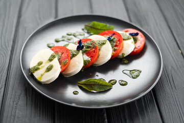 Italian caprese salad with tomatoes, mozzarella cheese, basil, olive oil served on black plate over dark wood background