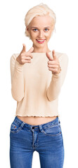 Young blonde woman wearing casual clothes pointing fingers to camera with happy and funny face. good energy and vibes.