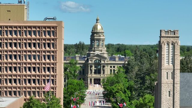 State capitol building of capital of Wyoming, Cheyenne. Aerial rising shot with telephoto lens. American flag waving next to high rise building and church.