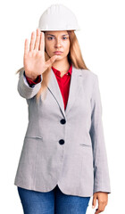 Beautiful young woman wearing architect hardhat doing stop sing with palm of the hand. warning expression with negative and serious gesture on the face.