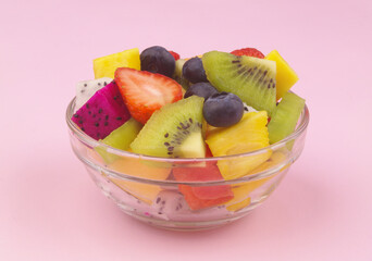 Fruit salad. Glass bowl with colorful sliced fruits on pink background.