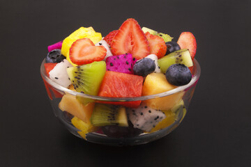 Colorful slices fresh fruits in glass bowl on black background
