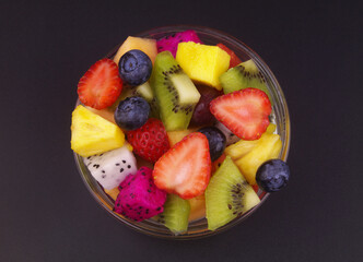 Top view of colorful fruit salad in glass bowl on black background.