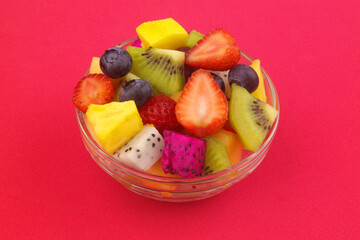 Bowl with colorful sliced fruits on red background. 