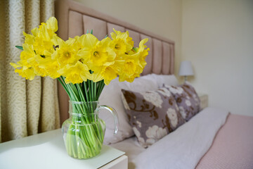 Bouquet of flowers in vase on bedside table in bedroom interior