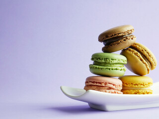 Colorful macarons stacked on small and decorative plate, light background and copy space.