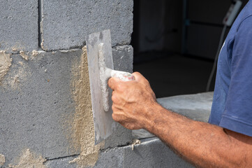 Maurer mit Kelle in der Hand mauert eine Hauswand auf der Baustelle
