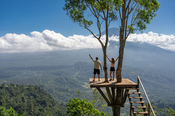 Couple of young people travellers enjoy vacation on Bali island, stand on the viewpoint with Agung volcano.