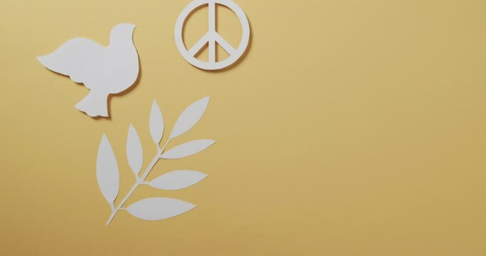 Close up of white dove with peace sign and leaf and copy space on yellow background