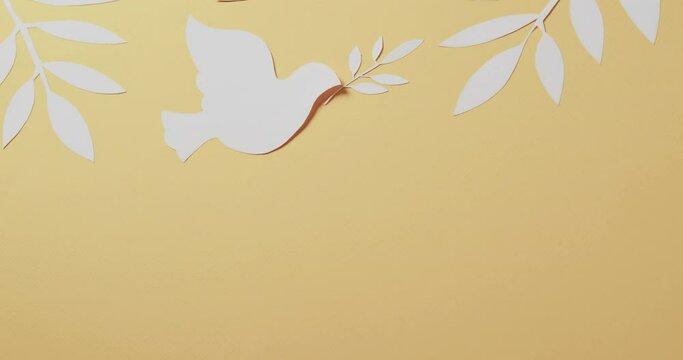 Close up of white dove with leaves and copy space on yellow background