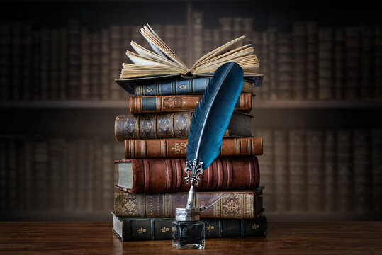 Old books ,quill pen and vintage inkwell on wooden desk in old library. Ancient books historical background. Retro style. Conceptual background on history, education, literature topics..