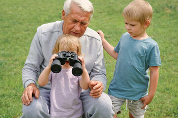 Grandfather and grandchildren using binoculars In Park. Happy family time. Old man grandpa playing...