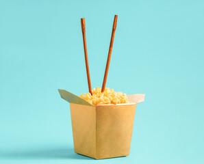 Egg noodles in cardboard box with chopsticks on blue background - Powered by Adobe