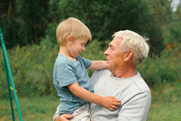 Grandfather and grandchild baby have fun during walk In Park. Happy family time. Old man grandpa hugging 4 years child boy at summer day. Smiling Senior male spending time with his grandson together.
