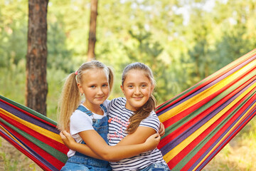 Fototapeta na wymiar Kids relax in colorful rainbow hammock. Hot day garden outdoor fun. Afternoon nap during summer vacation. Children relaxing.
