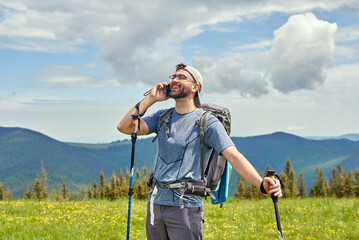 Fototapeta na wymiar Handsome man standing in the meadow, making a call and laughing. Mountains on the background. Activity and technology concept.