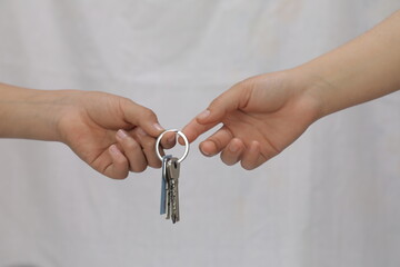 Hands of woman giving keys to a man on white background.