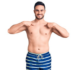 Fototapeta premium Young handsome man wearing swimwear looking confident with smile on face, pointing oneself with fingers proud and happy.
