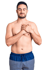 Young handsome man wearing swimwear smiling with hands on chest with closed eyes and grateful gesture on face. health concept.