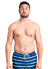 Fototapeta premium Young handsome man wearing swimwear puffing cheeks with funny face. mouth inflated with air, crazy expression.