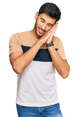Young handsome man wearing casual clothes sleeping tired dreaming and posing with hands together while smiling with closed eyes.