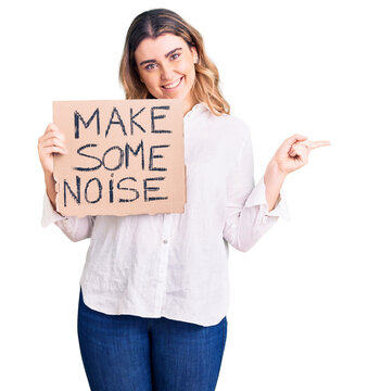 Young caucasian woman holding make some noise banner smiling happy pointing with hand and finger to the side