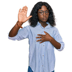Beautiful african young woman wearing casual clothes and glasses swearing with hand on chest and...