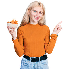 Young caucasian woman holding nachos potato chips smiling happy pointing with hand and finger to...