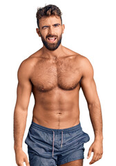 Young hispanic man wearing swimwear shirtless winking looking at the camera with sexy expression, cheerful and happy face.