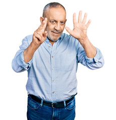 Senior man with grey hair and beard wearing casual blue shirt showing and pointing up with fingers number seven while smiling confident and happy.