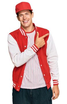 Handsome caucasian man wearing baseball uniform cheerful with a smile of face pointing with hand and finger up to the side with happy and natural expression on face