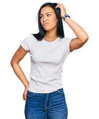 Beautiful hispanic woman wearing casual white tshirt confuse and wondering about question. uncertain with doubt, thinking with hand on head. pensive concept. - obrazy, fototapety, plakaty