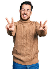 Naklejka premium Young hispanic man wearing casual clothes smiling with tongue out showing fingers of both hands doing victory sign. number two.