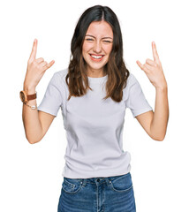 Young beautiful woman wearing casual white t shirt shouting with crazy expression doing rock symbol with hands up. music star. heavy music concept.