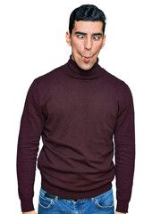 Handsome hispanic man wearing casual turtleneck sweater making fish face with lips, crazy and comical gesture. funny expression.