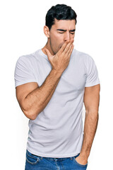 Handsome hispanic man wearing casual white t shirt bored yawning tired covering mouth with hand. restless and sleepiness.