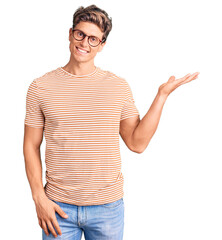 Young handsome man wearing casual clothes and glasses smiling cheerful presenting and pointing with palm of hand looking at the camera.