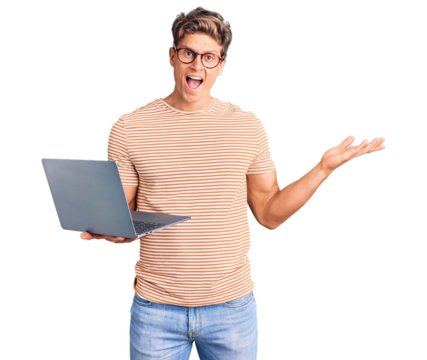 Young handsome man wearing glasses holding laptop celebrating victory with happy smile and winner expression with raised hands - Powered by Adobe