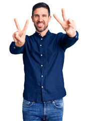 Fototapeta premium Young handsome man wearing casual shirt smiling with tongue out showing fingers of both hands doing victory sign. number two.