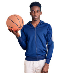 Young african american man holding basketball ball thinking attitude and sober expression looking self confident