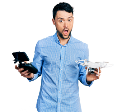 Hispanic man with beard using drone with remote control in shock face, looking skeptical and sarcastic, surprised with open mouth